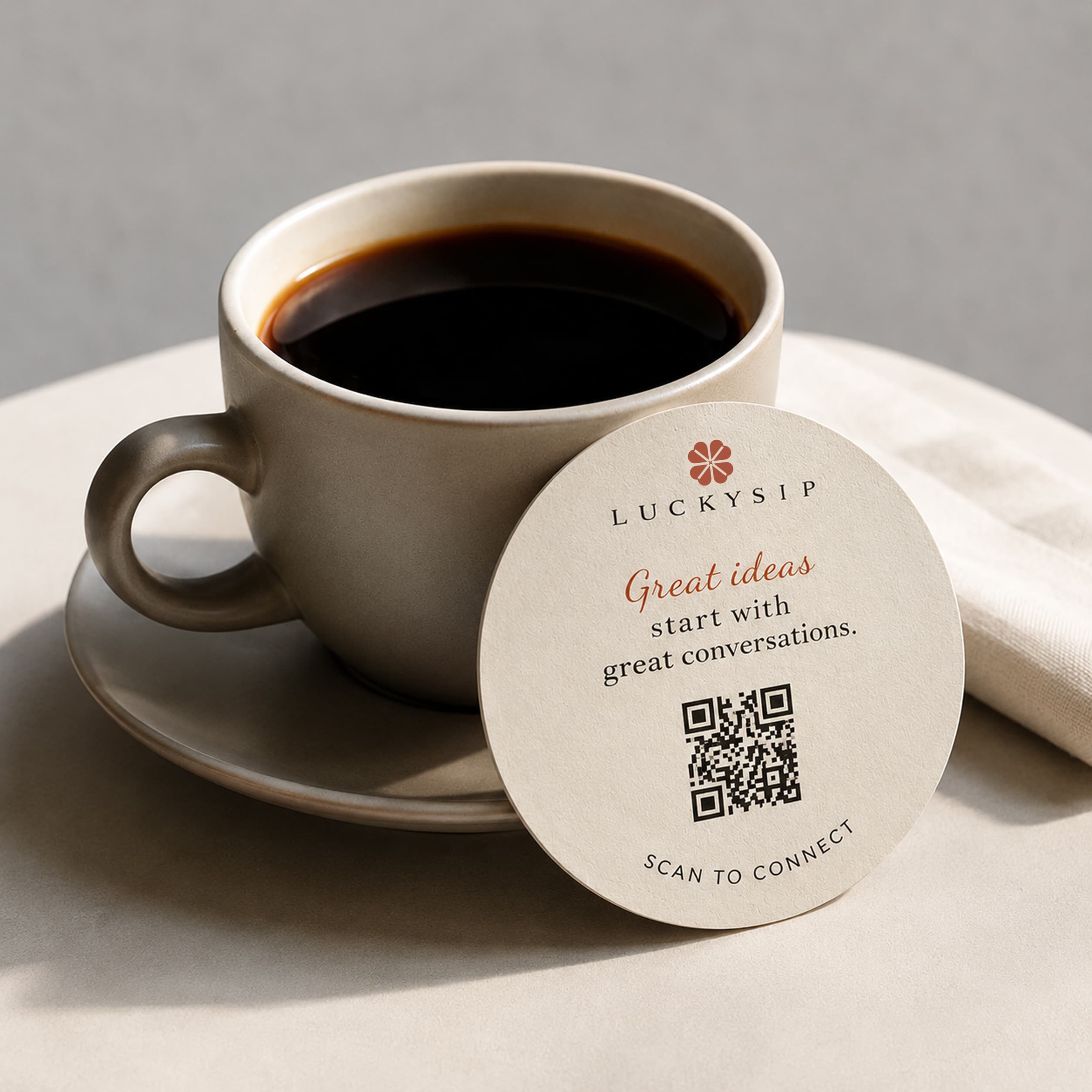 A coffee cup with a LuckySip QR coaster on a saucer.