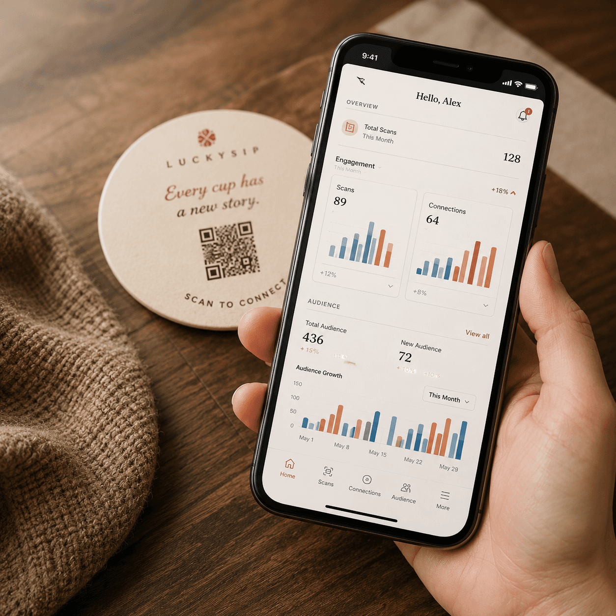 A hand holding a phone showing a chart dashboard beside a LuckySip coaster.